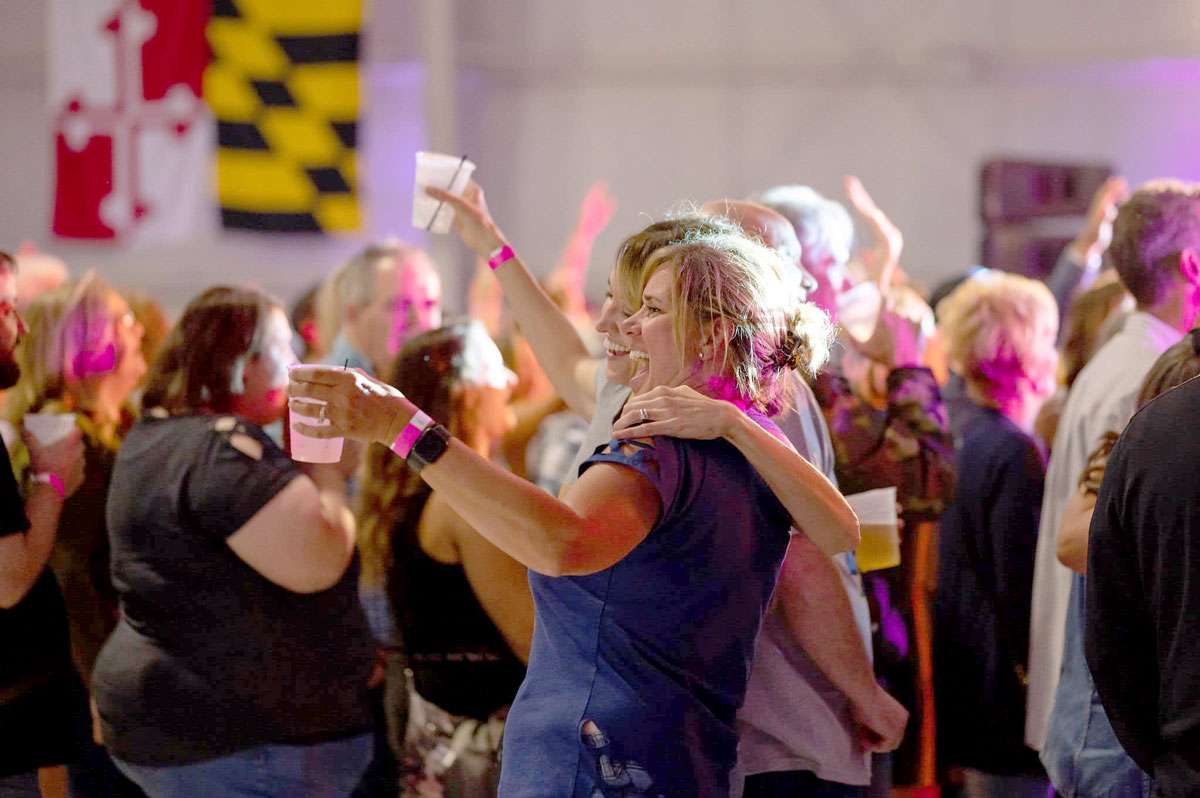 two women enjoying a concert with drinks in hand and a Maryland flag in the background