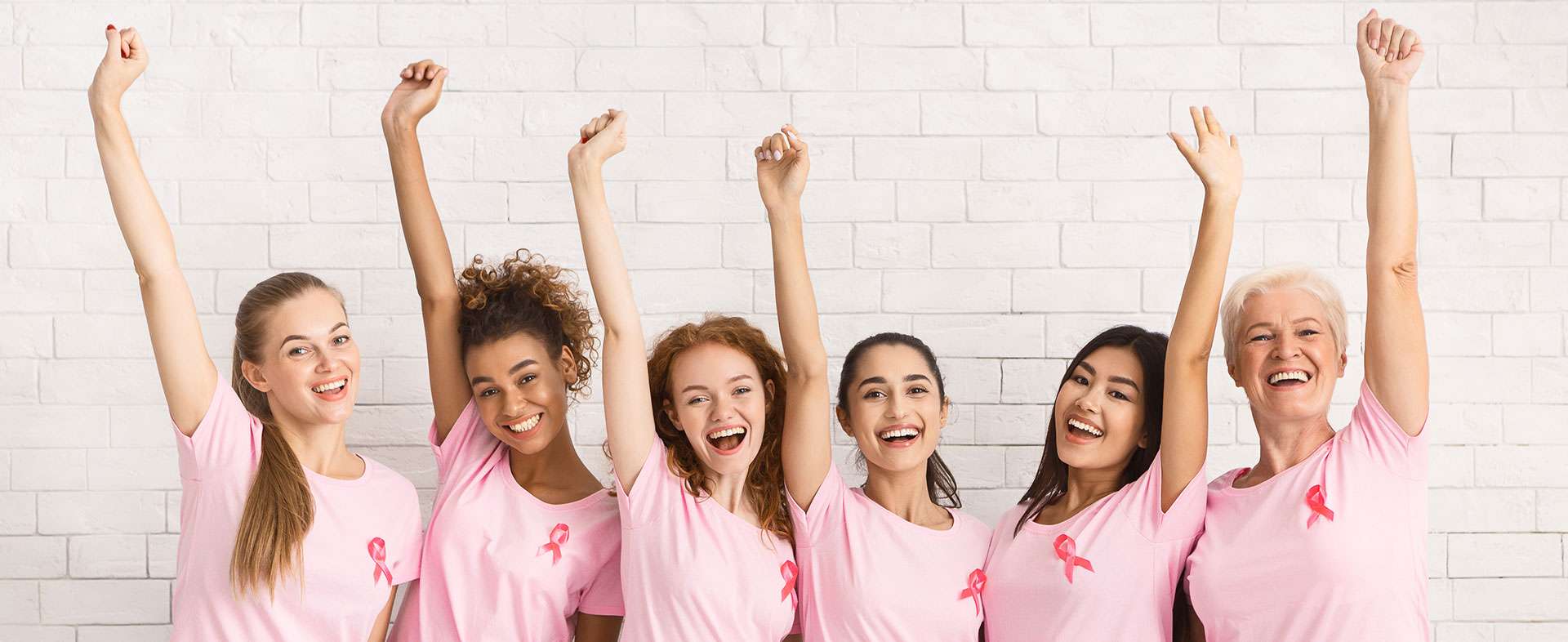 group of smiling women in pink t-shirts with fists in the air supporting breast cancer