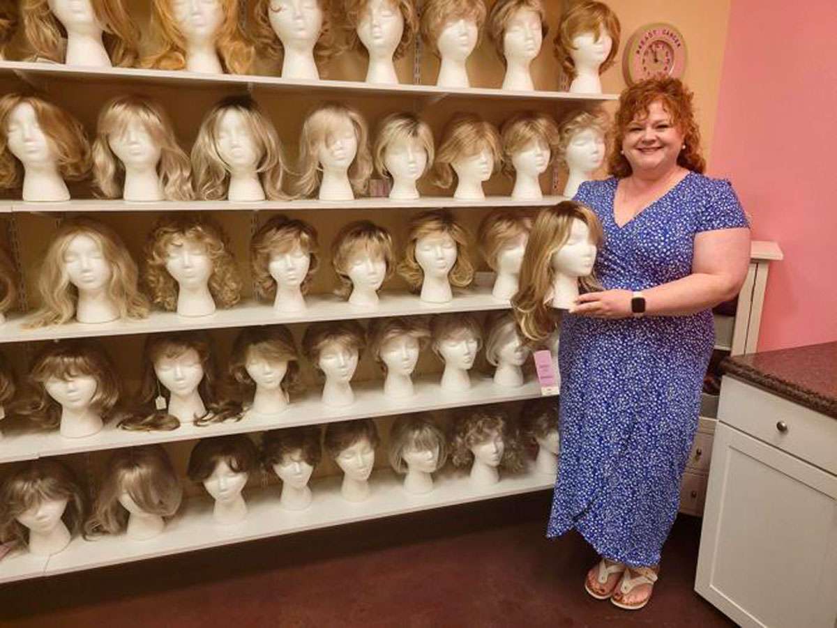 BCA executive director posing with a wall display of women's wigs'